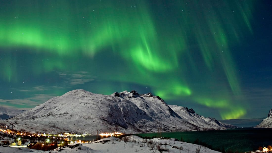 Nordlys som lyser over snøkledd fjelltopp i vintermørket i Tromsø