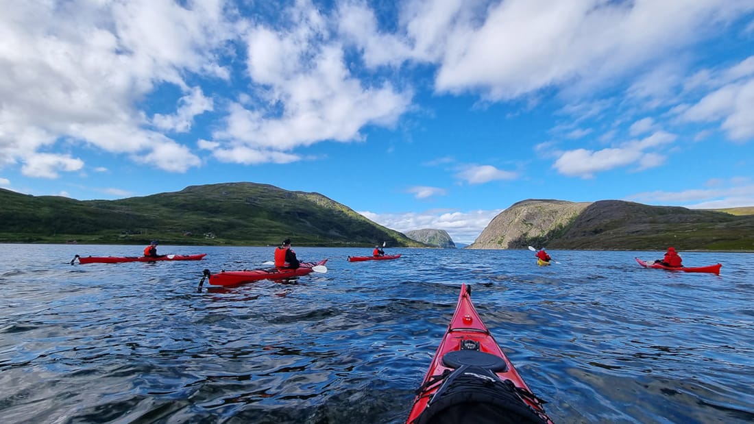 Person padler i rød kajakk i norske fjorder.