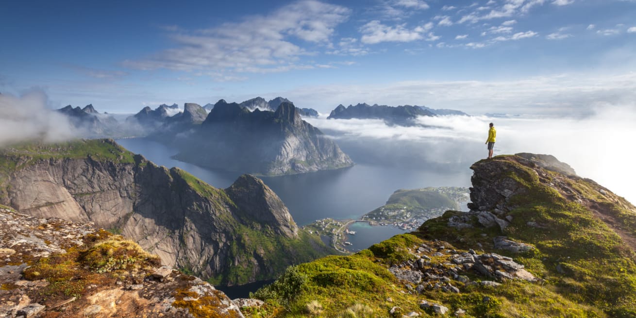 Mann som st&aring;r p&aring; en fjelltopp i Lofoten og ser utover fjell og hav.