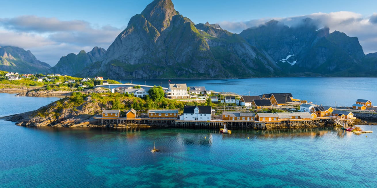 &Oslash;y med gule hus, omgitt av bl&aring;tt hav og fjellandskap i Lofoten.